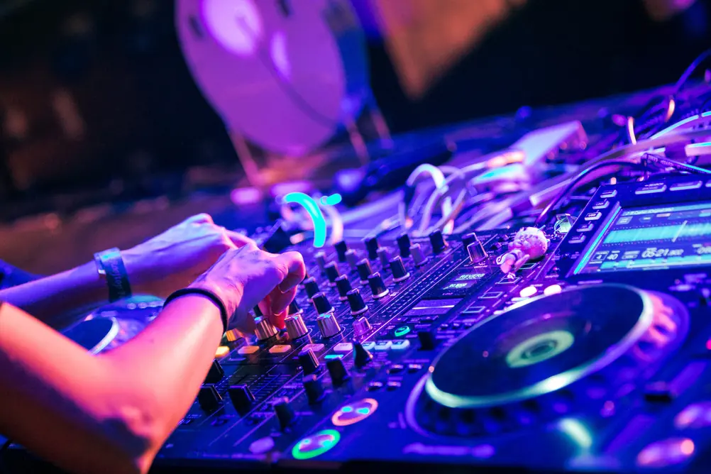 A DJ's hands on the decks under purple light