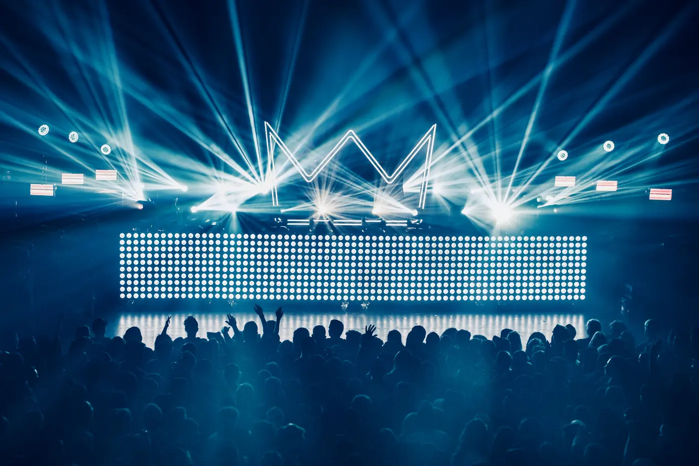 A lighting show of beams and LED panels over a crowd