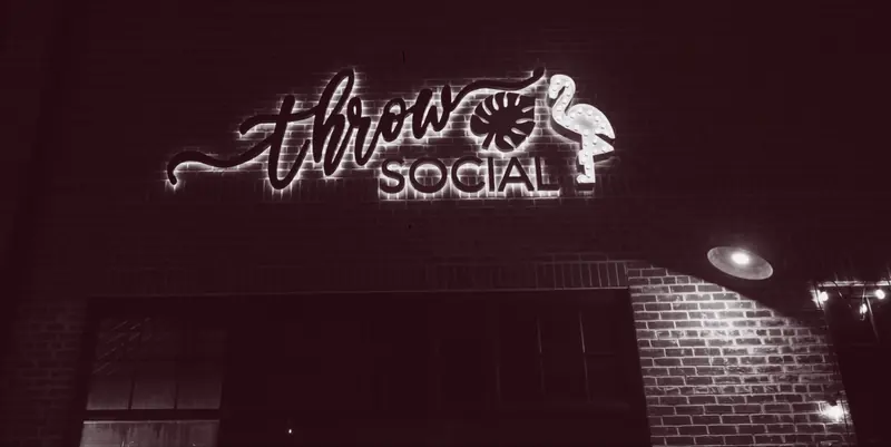 The THRōW Social neon sign over a brick wall